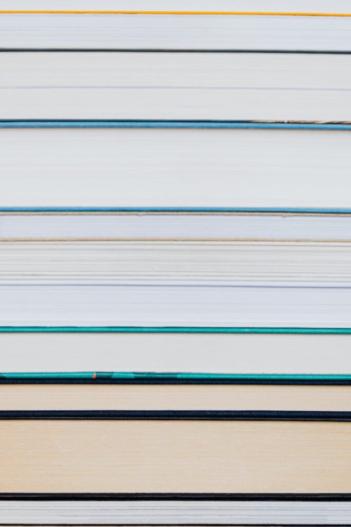 A close-up of a neatly stacked pile of hardcover books with visible spines.